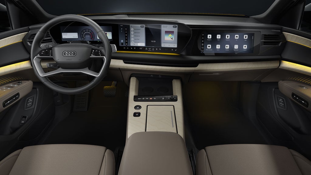 View from the back seat into the cockpit of the Audi Q9 SUV. In the foreground are the steering wheel and the panoramic displays featuring the Audi Virtual Cockpit and the MMI display.