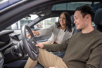 Side profile view of a man in the drivers seat looking at the wheel smiling, while a woman points out details of the vehicle smiling.