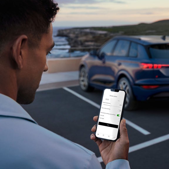 Over-the-shoulder view of a person using the cabin pre-conditioning feature in the myAudi app on their smartphone.