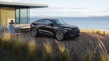 Three-quarter side view of the Audi SQ6 Sportback e-tron parked and charging by a waterfront home.