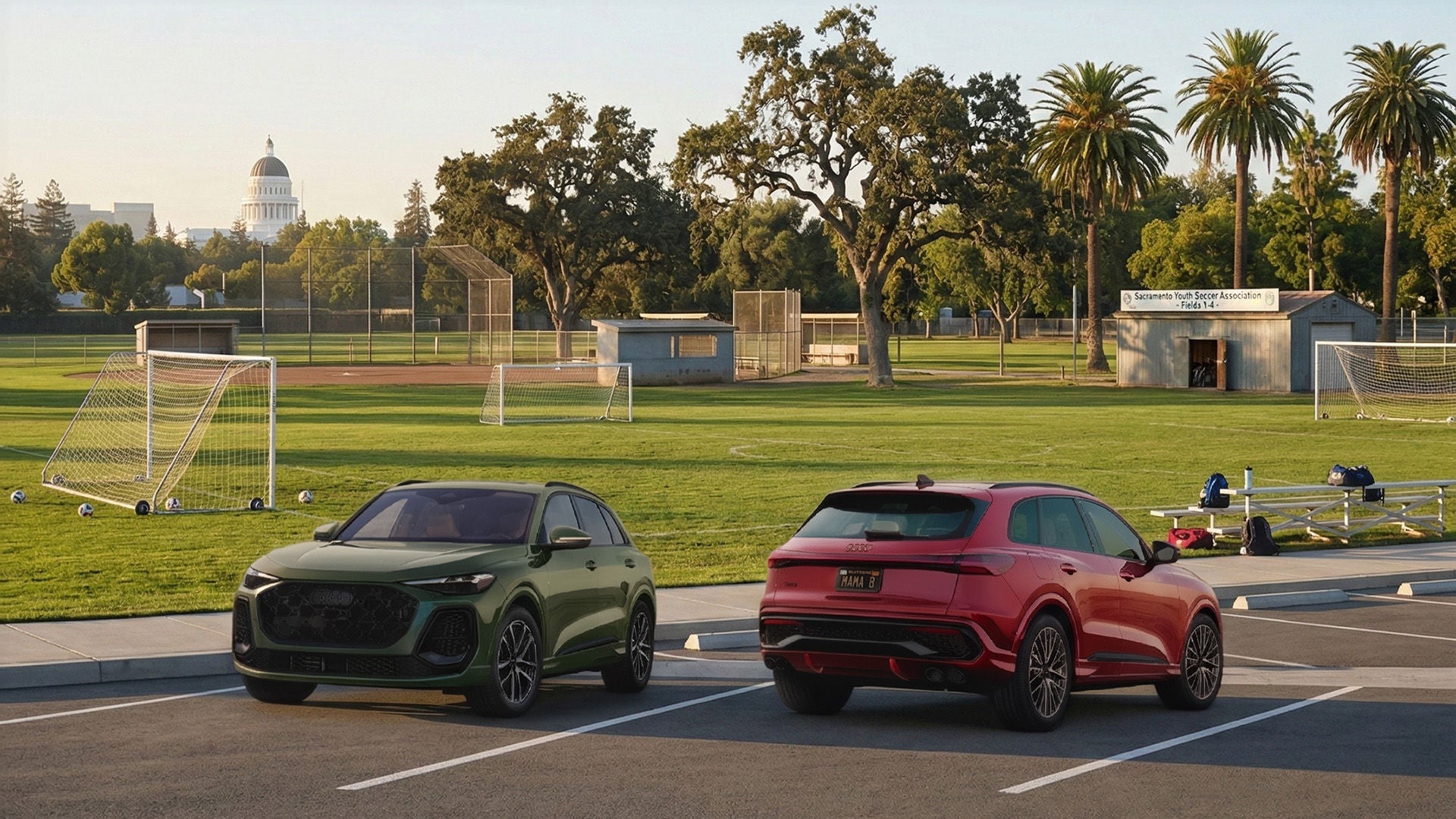 An Audi Q5 and Q5 Sportback parked next to each other by a soccer field.