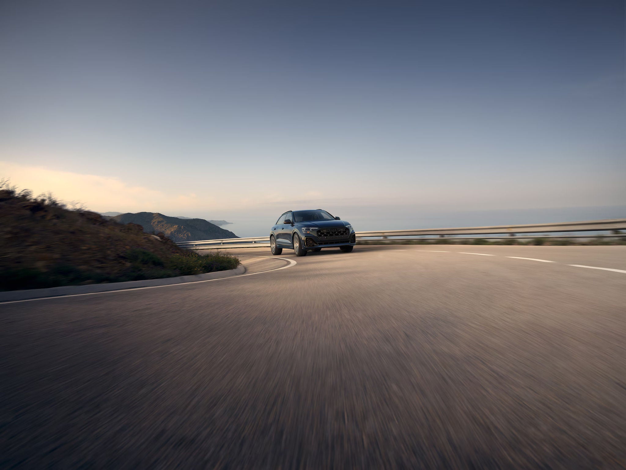 New 2025 Audi Q8 SUV cruising on a banked hilly road.