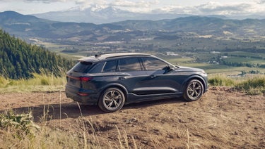 Three-quarter side view of the Audi Q6 e-tron parked by a modern home.