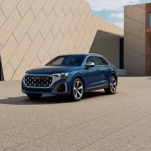 Three-quarter front view of the Audi SQ8 parked by a modern building.