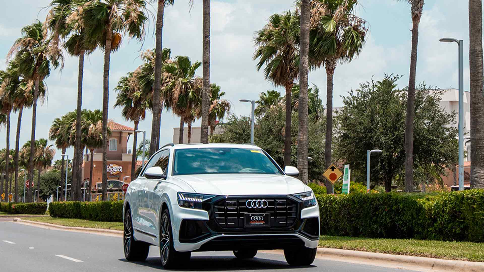 Front view of an Audi accelerating on a road near palm trees
