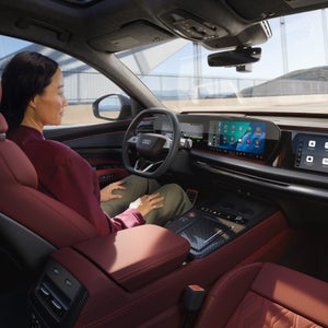 Close-up of a display in the vehicle interior. The silhouette of a vehicle travelling straight ahead is shown. To the left is a text box providing information about assisted hands-free driving.