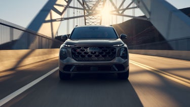 A front view of the Audi SQ7 SUV on a bridge. The low-hanging sun illuminates the scene behind the vehicle.