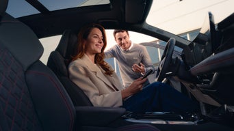 Audi employee and customer having a conversation while customer is seated in Audi vehicle driver's seat.