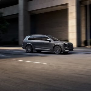 Grey Audi SQ9 driving through a modern city street, shown from the side profile.