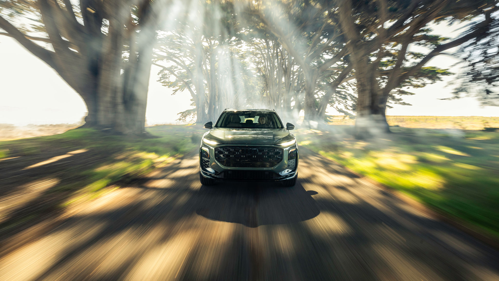 Silver Audi Q3 driving on an open dirt road with trees in the backgound.