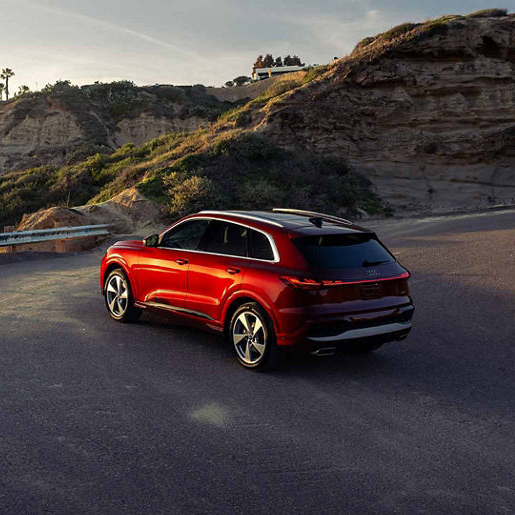 Red Audi driving up winding road at sunset