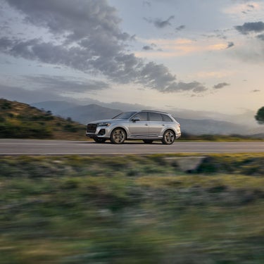 Side view of the Audi Q7 accelerating on a tree-lined road.