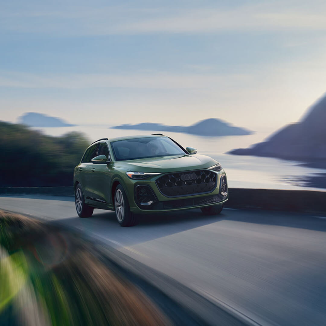 Front three-quarter view of a green Audi Q5 driving along a scenic coastal highway.