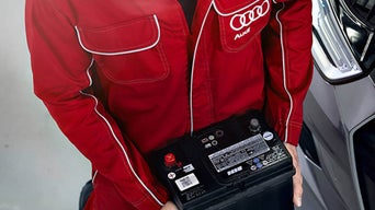 Service technician replacing a battery on an Audi vehicle.