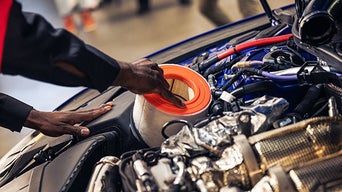 Service technician servicing vehicle with hood open.