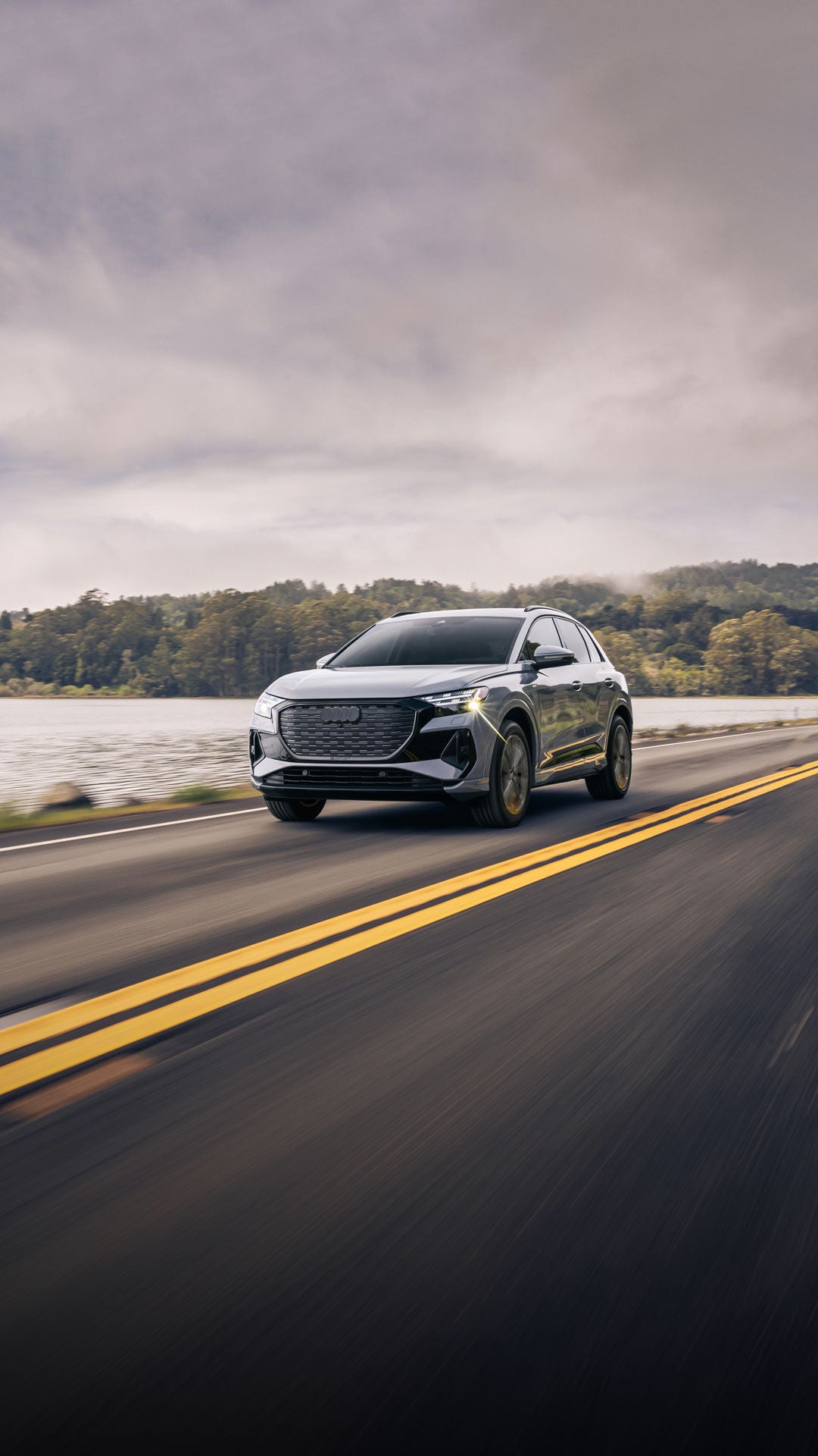 Three-quarter front view of the Audi Q4 e-tron accelerating on a waterside road.