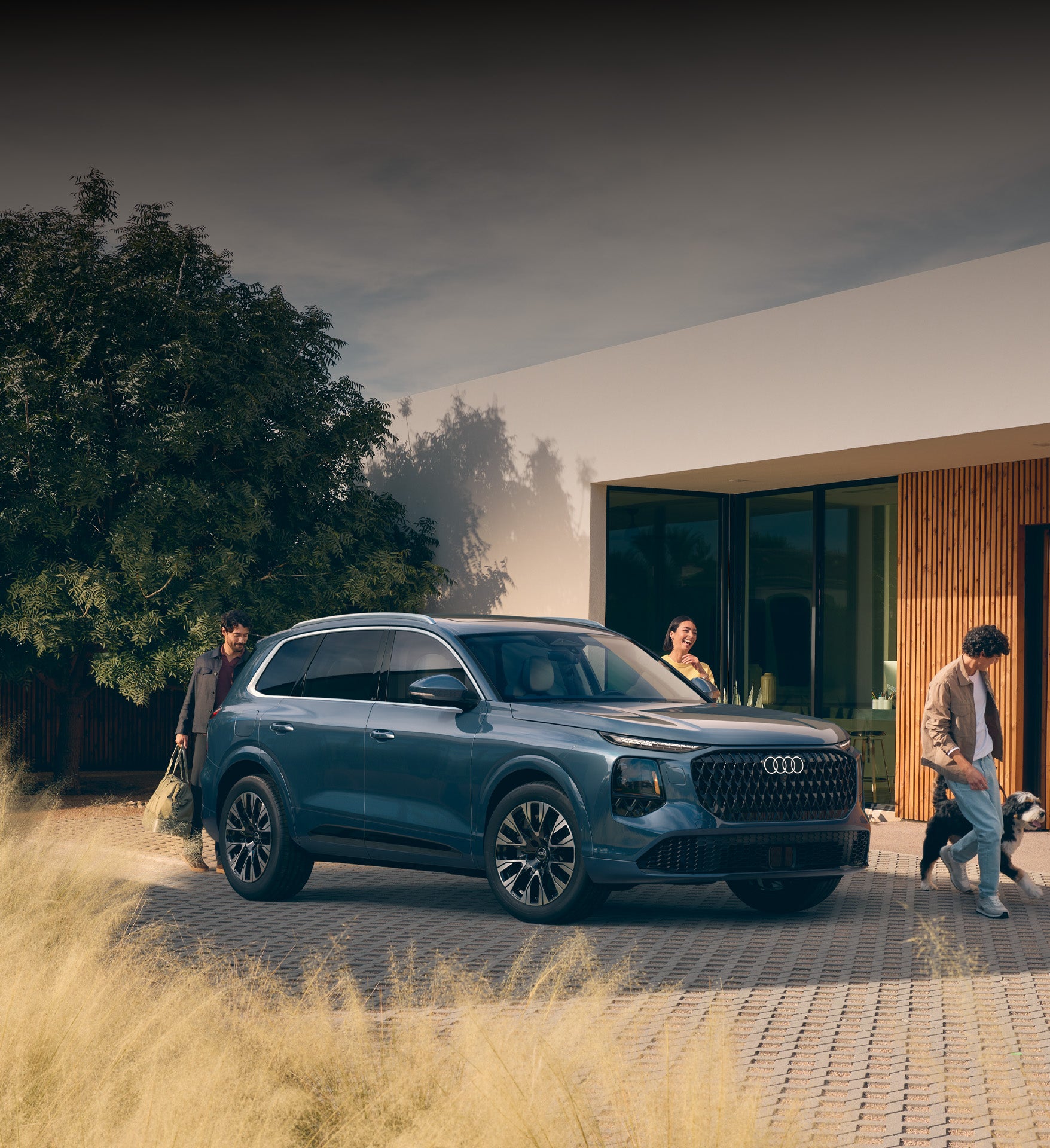 2027 Audi Q7 left front profile in front of building with family