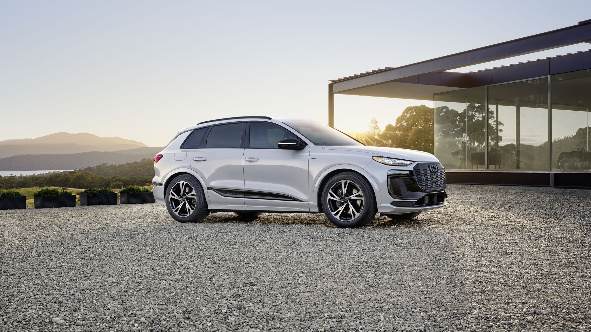 White q6 e-tron on gravel with a sunset and mountains in the background. 