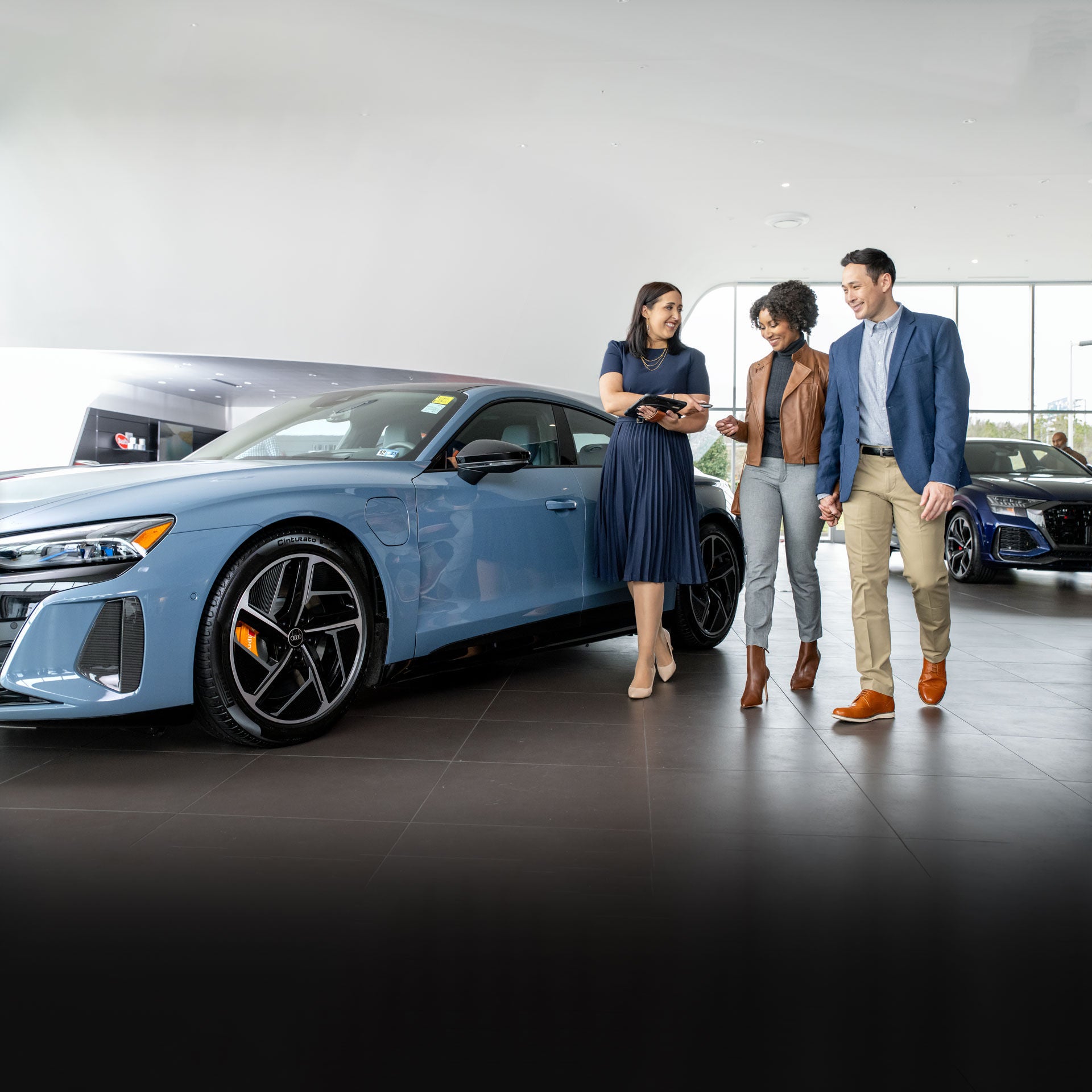 An Audi dealer showing a well-dressed couple to their new Audi e-tron GT.
