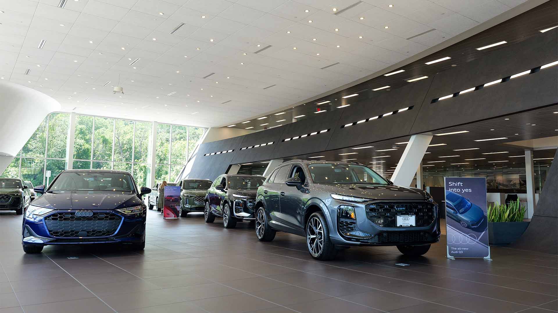 Audi sales specialist walking with a customer through the showroom. The sales specialist is handing the customer a key fob for an Audi vehicle.