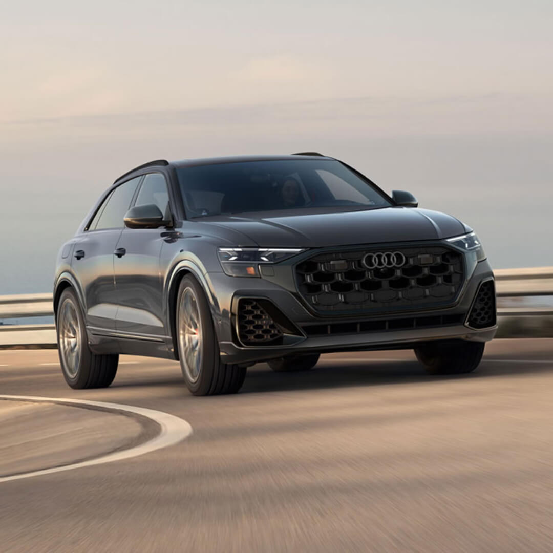 A front view action shot of a gray Audi SQ8 handling a sharp corner on a hazy seaside highway.