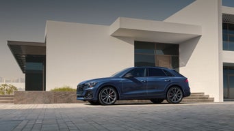 Side view of the Audi Q8 parked by a modern home.