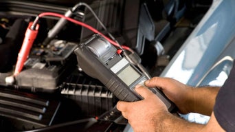 Service technician inspecting battery of Audi vehicle with hood open.