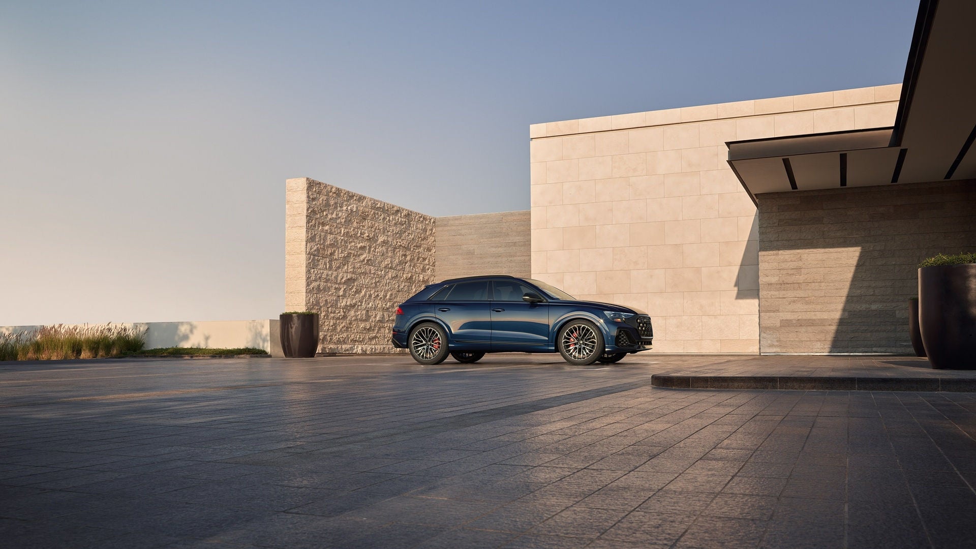 Blue Audi Q8 parked in front of a building structure made with various sizes of brick.