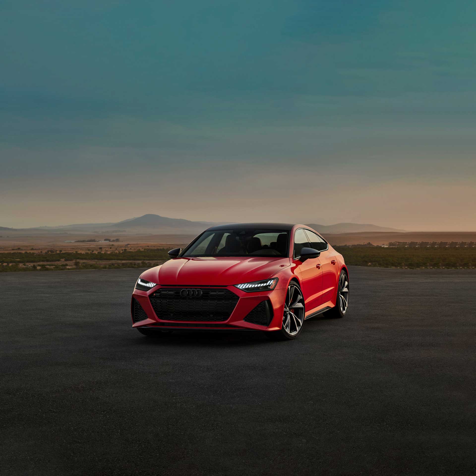 Front-view of a red Audi RS 5 Sportback parked on a road with mountains and bushes in the background.