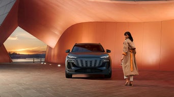 Front facing view of an Audi SQ6 e-tron parked, with a woman walking toward it.