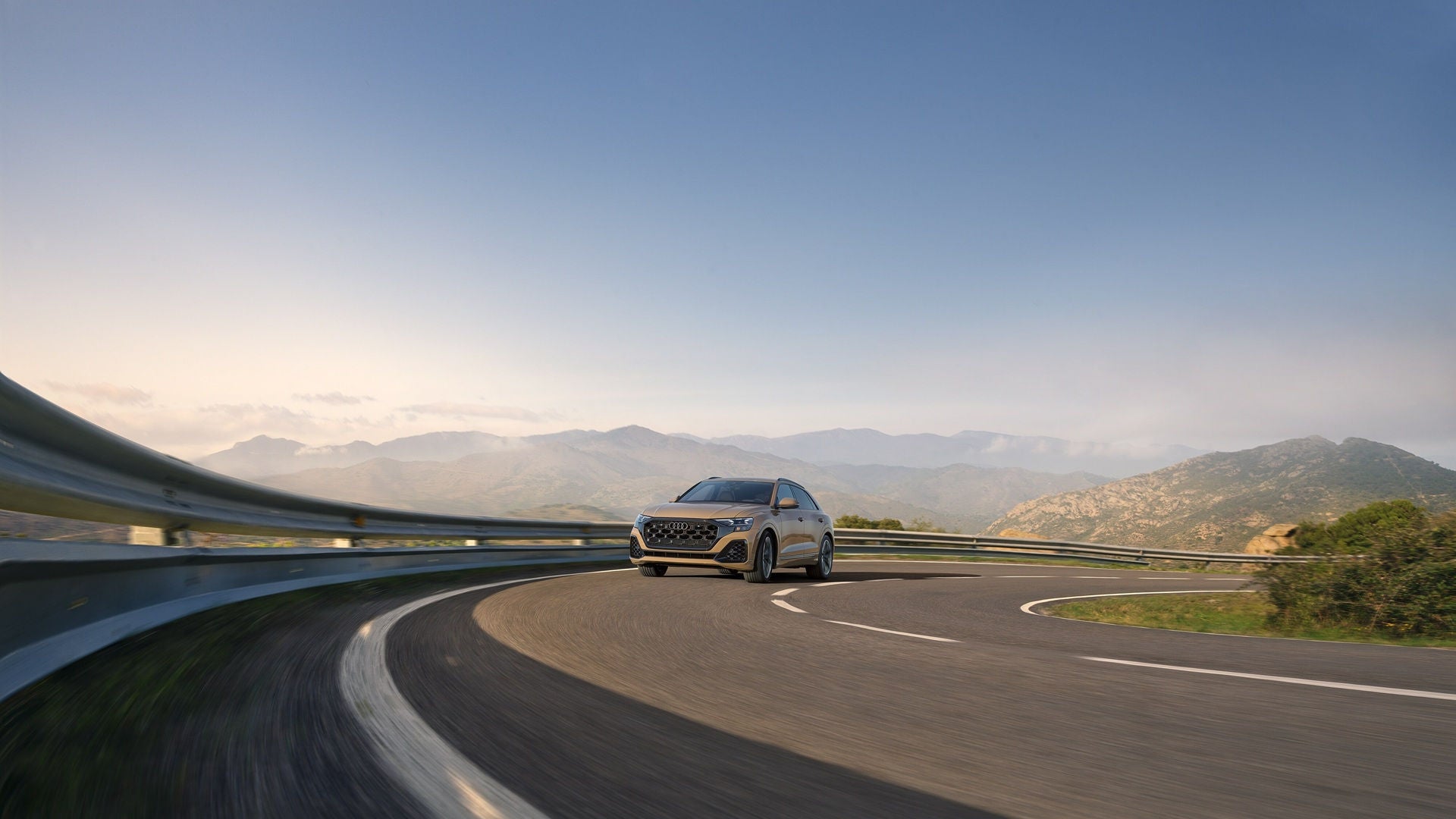 Silver Audi Q8 driving on an open road during the day with mountains in the background.