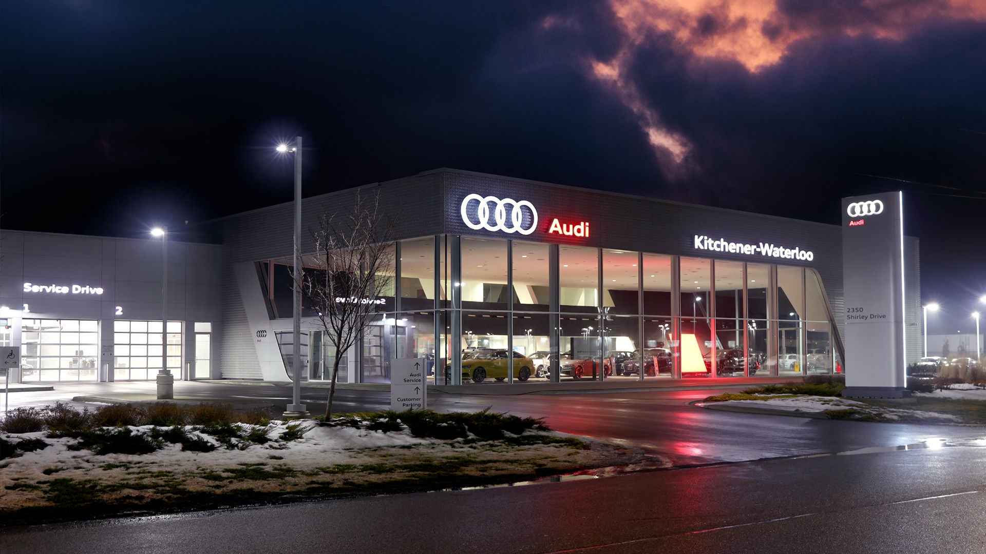 Audi sales specialist walking with a customer through the showroom. The sales specialist is handing the customer a key fob for an Audi vehicle. 