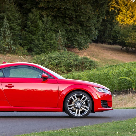 Side view of a red Audi TT Coupe parked in front of a grassy hill.
