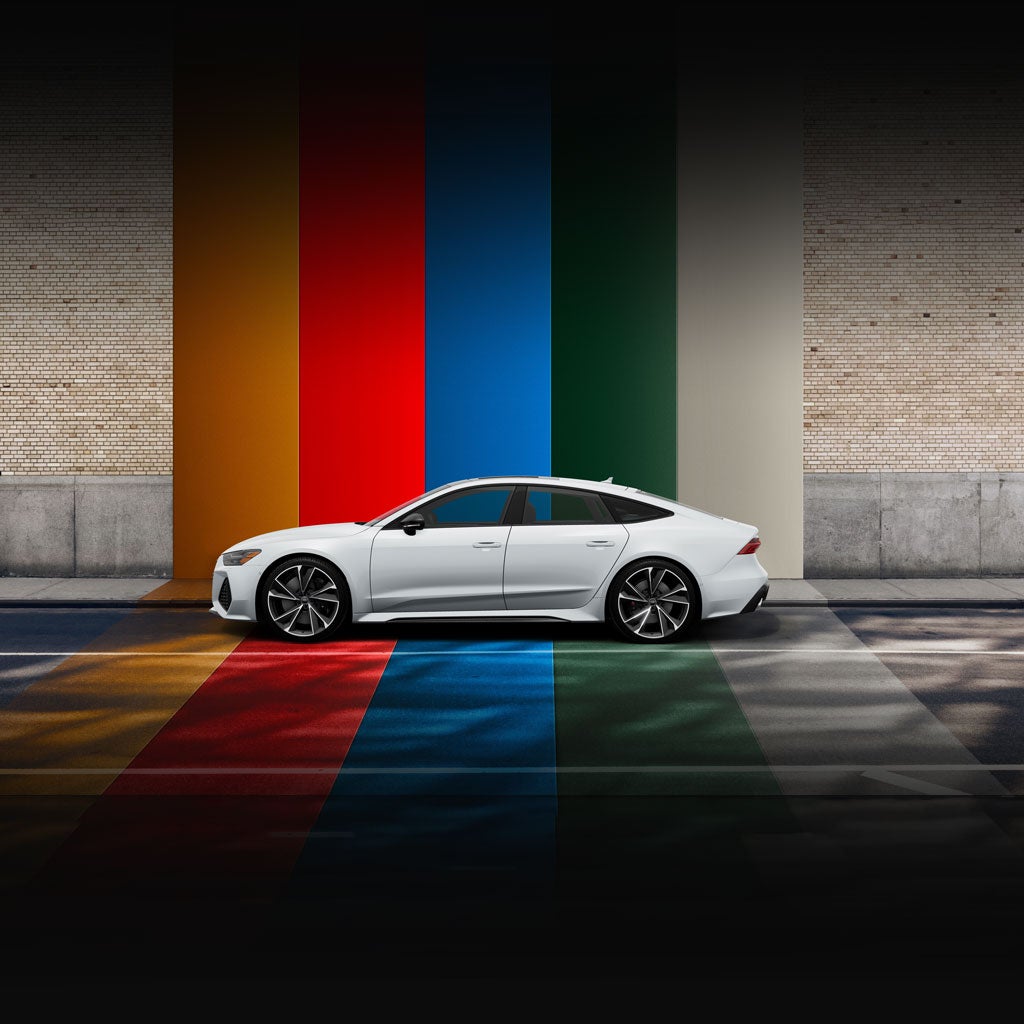 Side profile of a silver Audi RS 7 parked in front of a brightly-striped wall. 