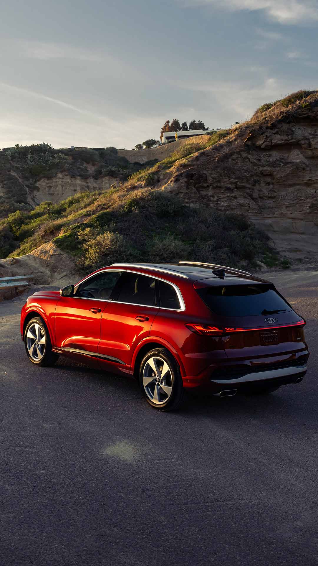 Red Audi driving up winding road at sunset.
