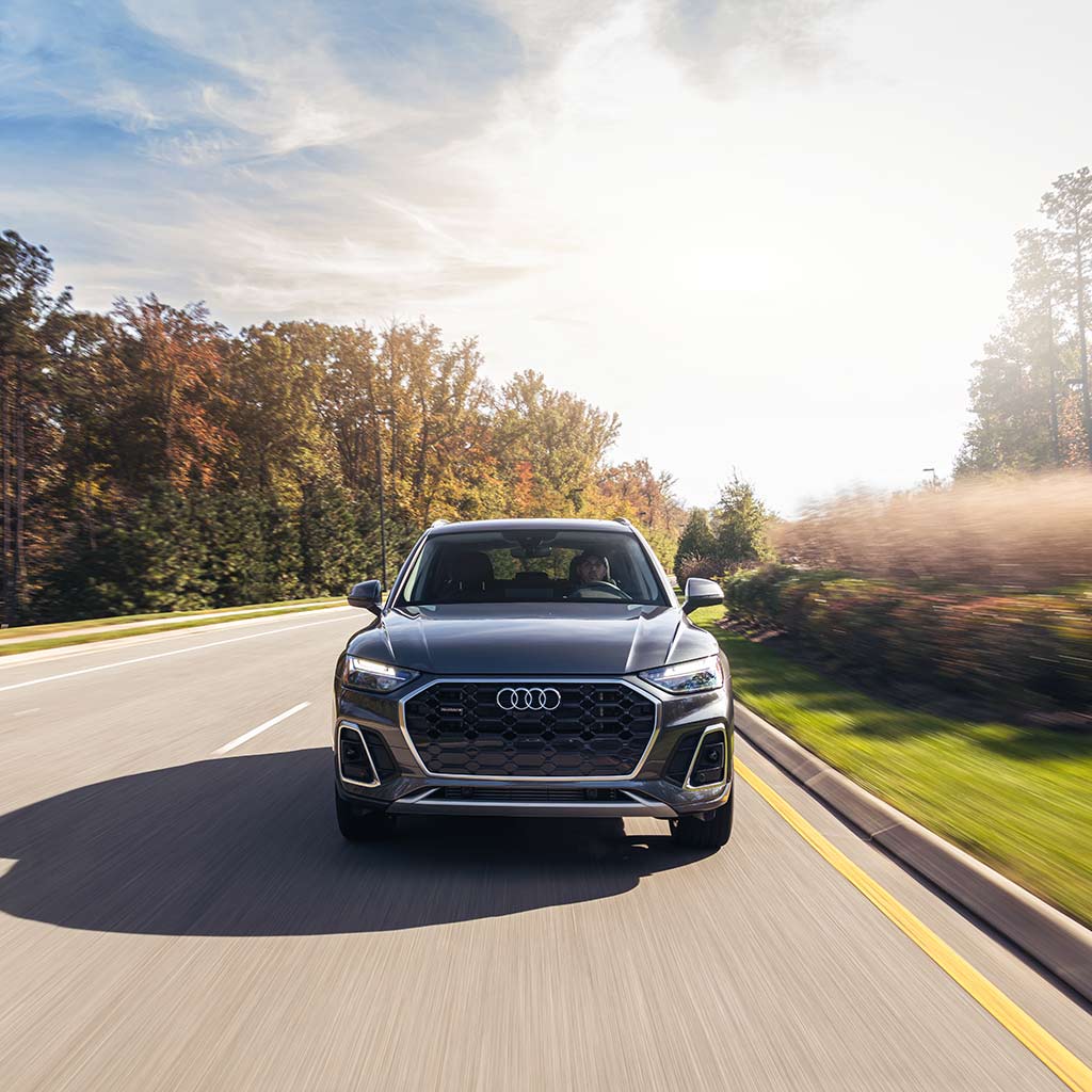 Front view of an Audi Q5 PHEV driving down a sunny, tree-lined road.