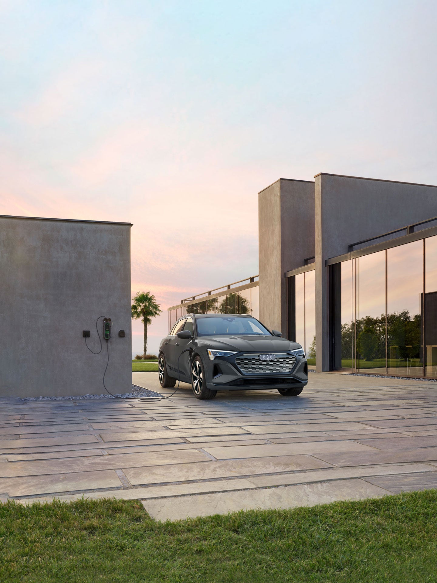 Three-quarter front profile of a gray Audi Q8 e-tron parked and charging on a driveway. 