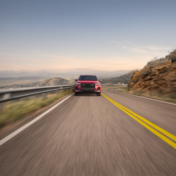 Front profile of a red Audi SQ7 accelerating on a mountain-side road.