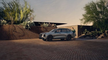 Side profile of the Audi SQ7 parked on a driveway of a modern home with a person opening the trunk.