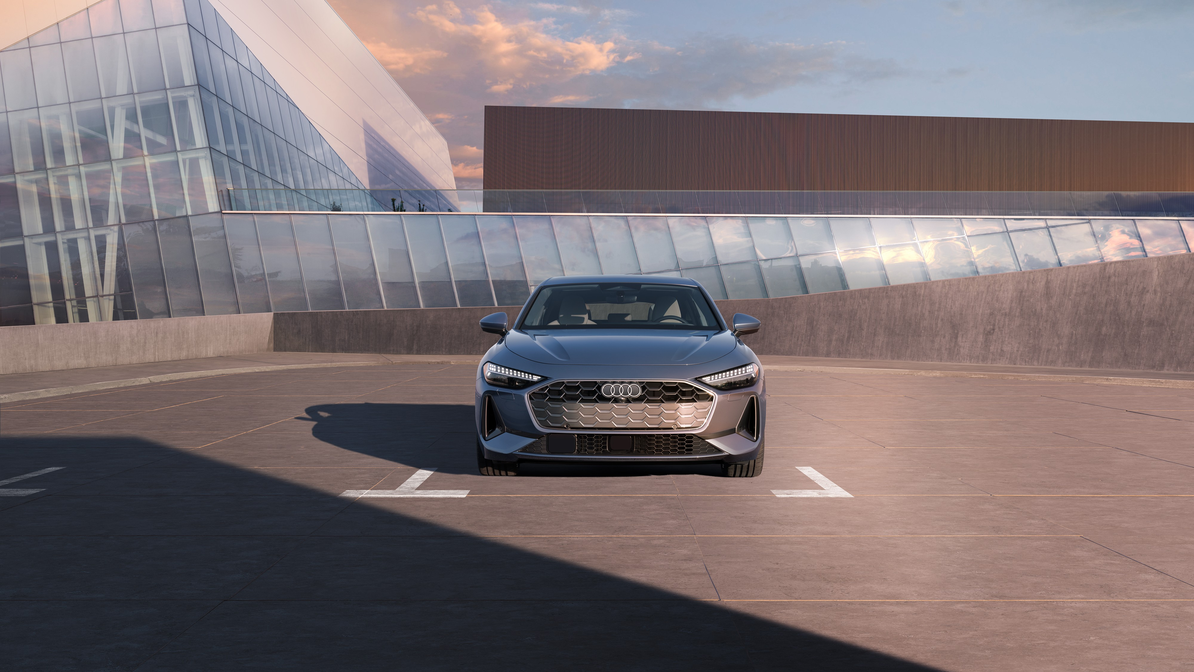 Silver audi a5 parked in an outdoor parking area with a glass building behind.