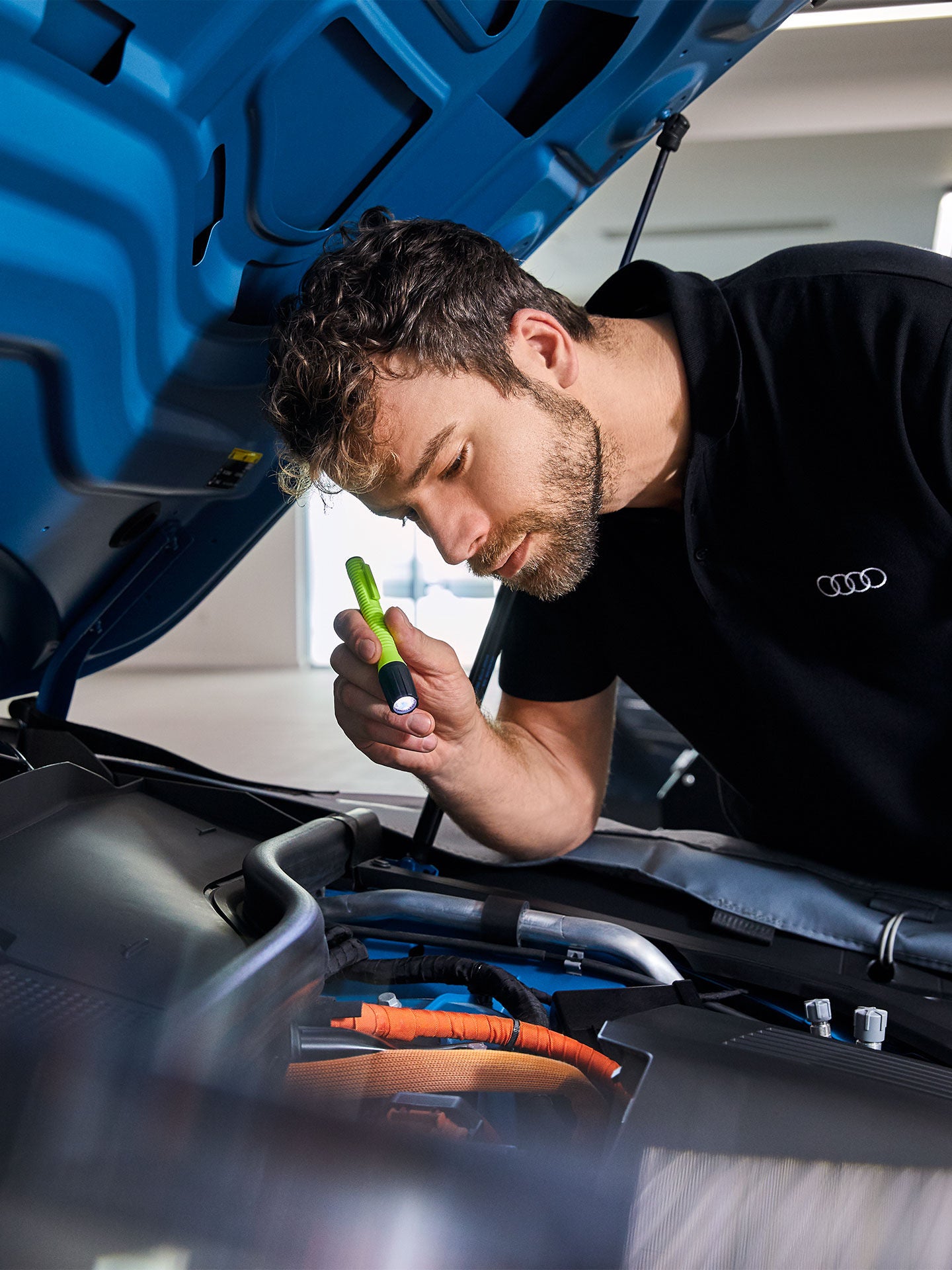 Service technician inspecting under the hood of a car with a flashlight.