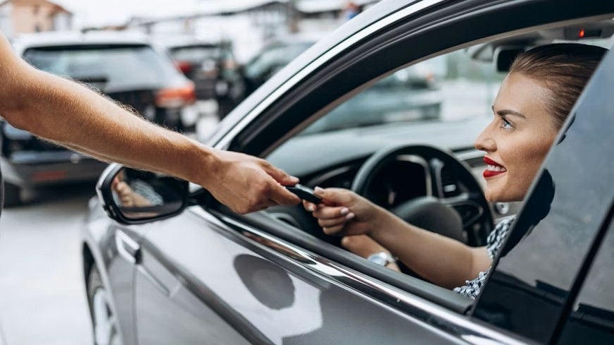 Woman sitting in driver's seat being handed car keys.