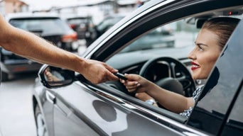 Woman sitting in driver's seat being handed car keys.