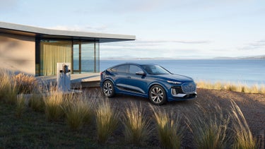 Three-quarter side view of the Audi SQ6 Sportback e-tron parked and charging by a waterfront home.