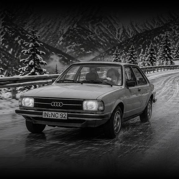 Three-quarter front view of an early Audi vehicle accelerating on a snowy road.