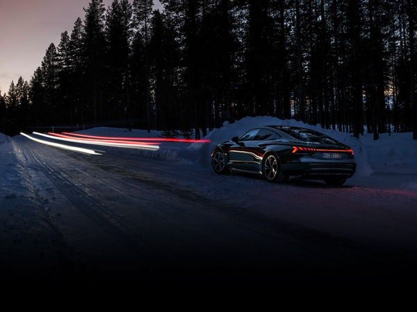 Long-exposure shot of an Audi RS e-tron GT driving on a snowy road at night, with light beams ahead. 