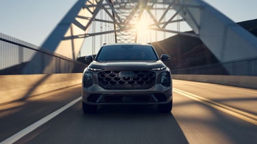 A front view of the Audi SQ7 SUV on a bridge. The low-hanging sun illuminates the scene behind the vehicle.