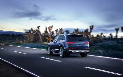 Dark blue Audi SUV driving down a desert road at dusk.