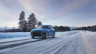 Three-quarter front view of the Audi SQ6 e-tron accelerating on a winter landscape.