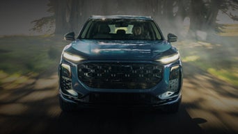 Front exterior action shot of a dark blue 2027 Audi Q3 driving down a tree-lined road.